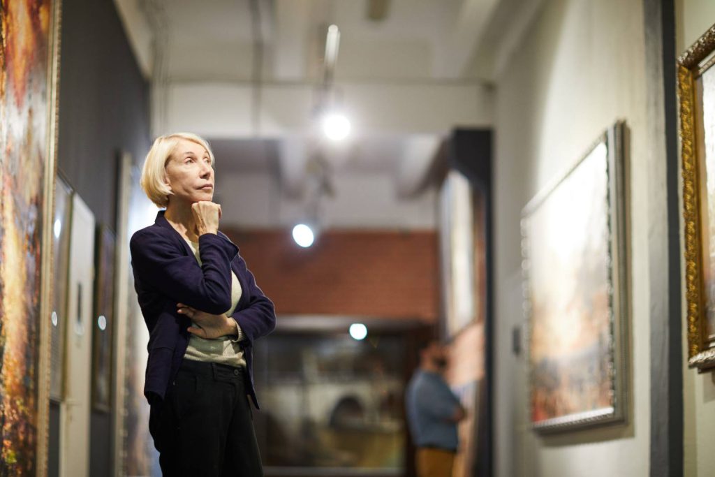 A woman studying paintings in a gallery, chin resting on her hand