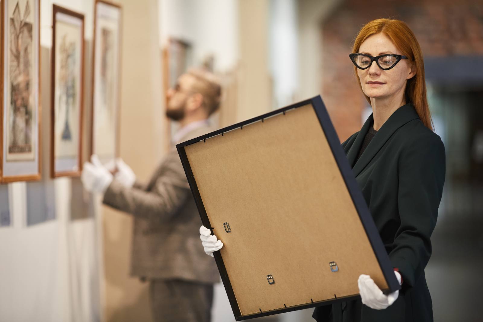Gallery staff in white gloves handling framed artworks for hanging