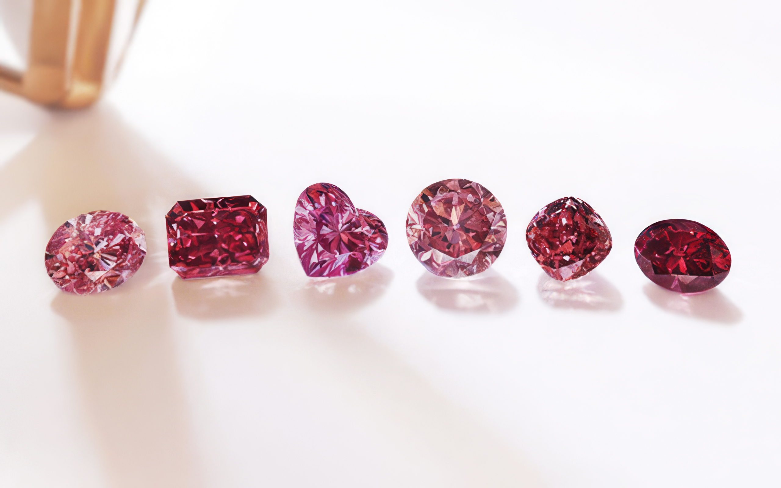 Six pink and red diamonds in different cuts lined up on a pale surface