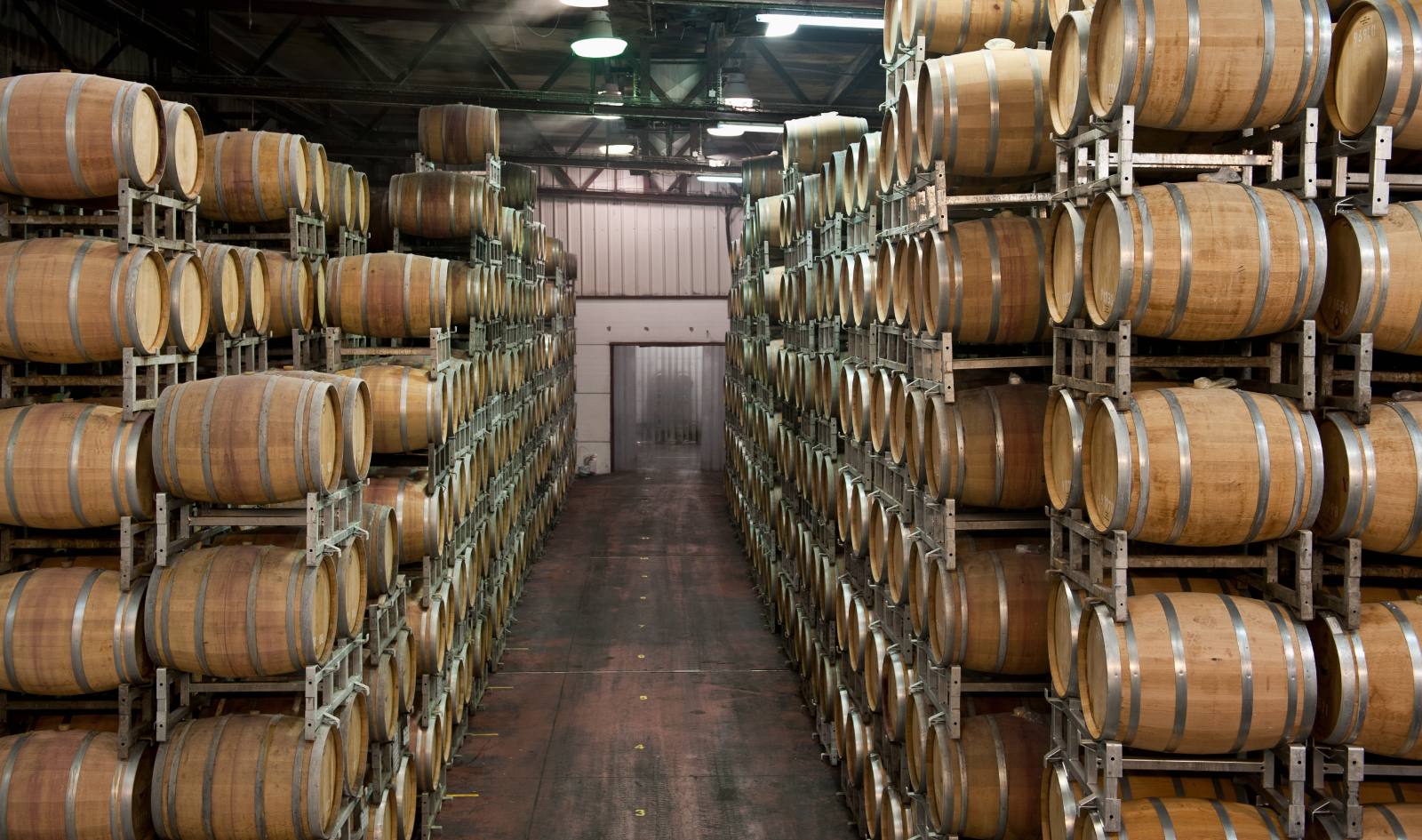 An aisle of oak casks racked floor to ceiling in a warehouse