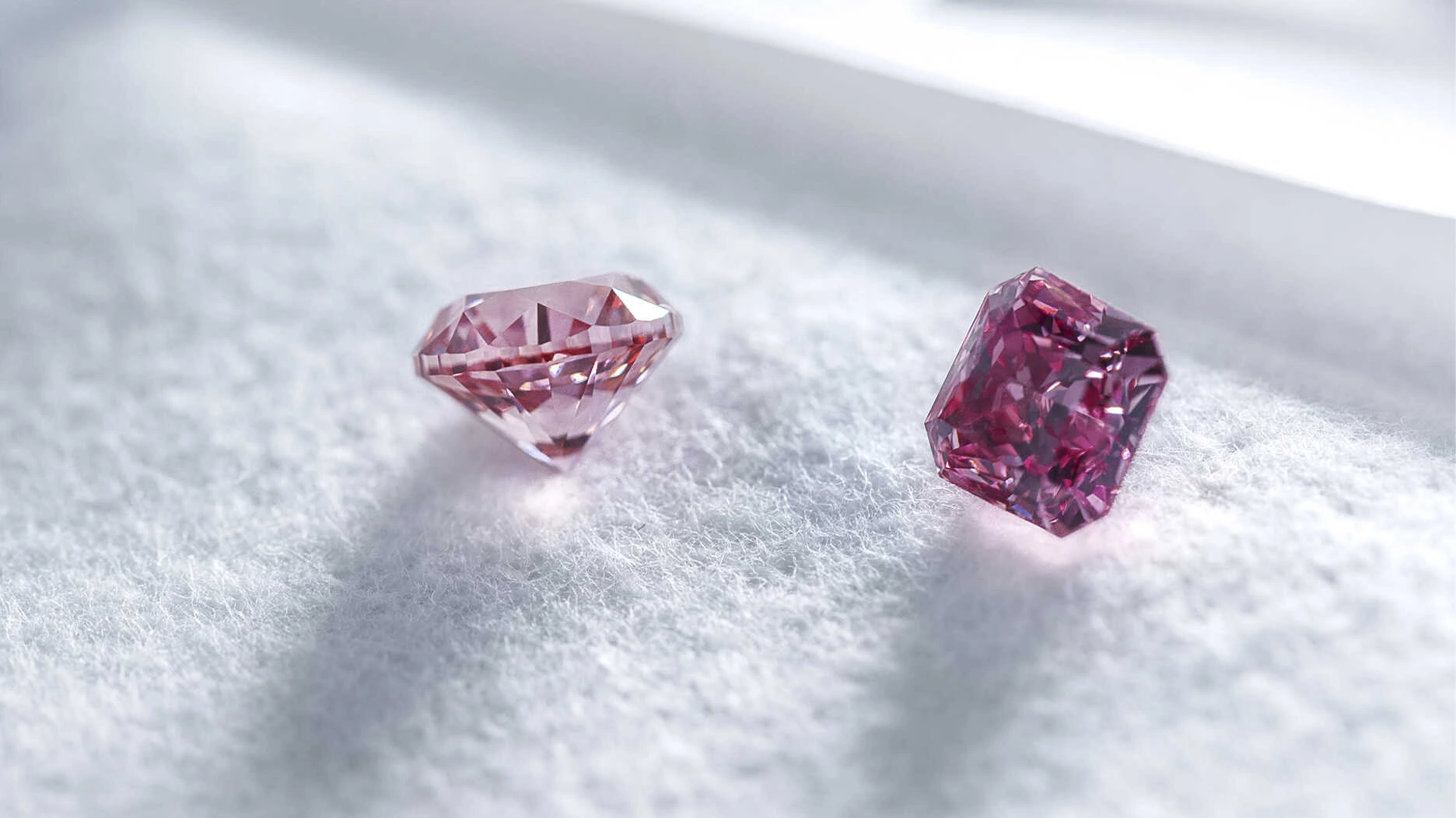Two loose polished pink diamonds resting on white fabric