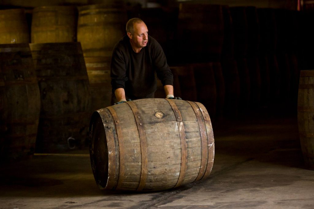 A warehouse worker rolling an oak whisky cask across the floor