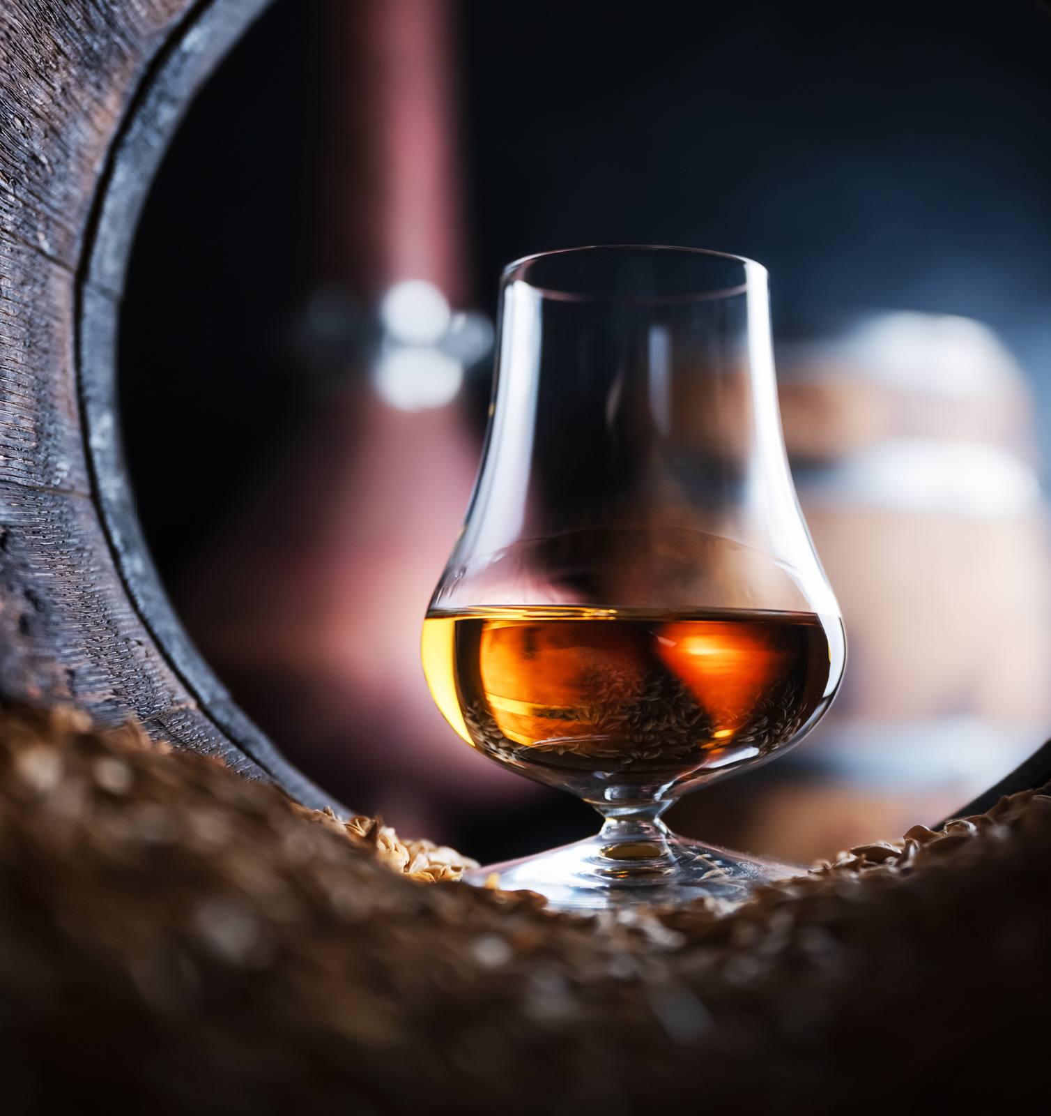 A glass of amber whisky framed inside the open end of an oak cask