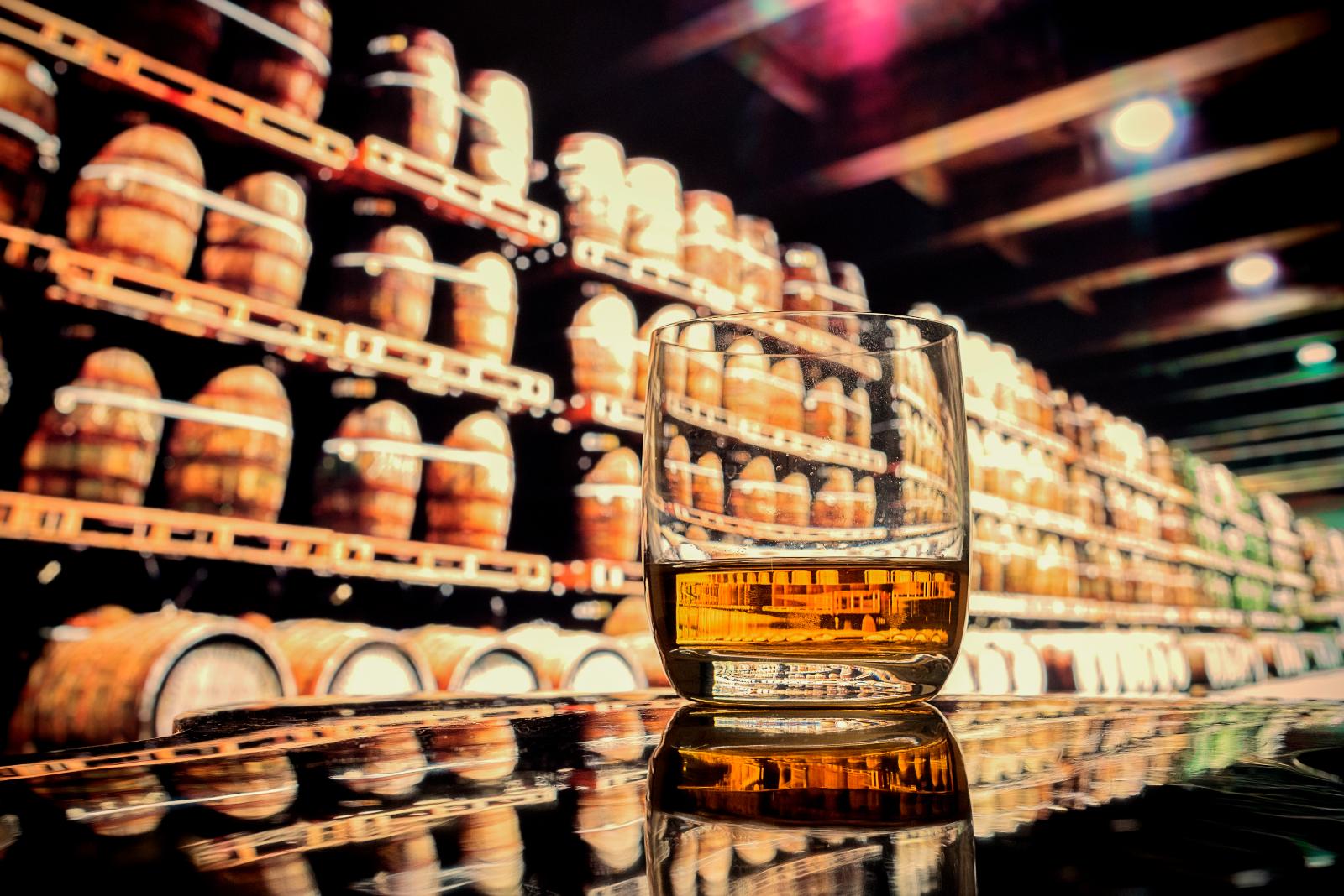 Glass of whisky in front of bonded warehouse casks